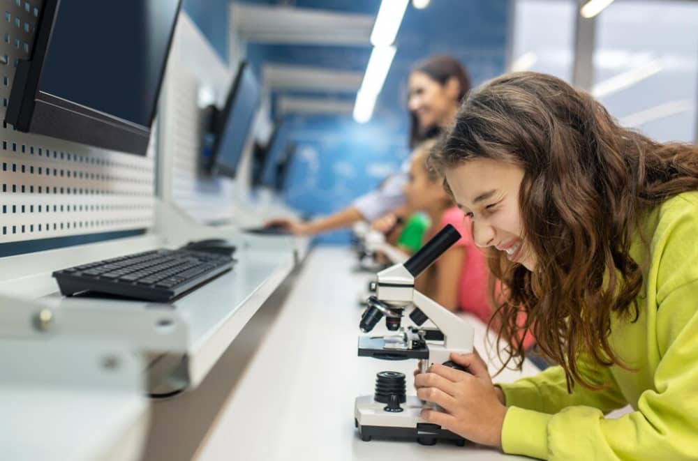 A girl smiles while using a microscope in a lab