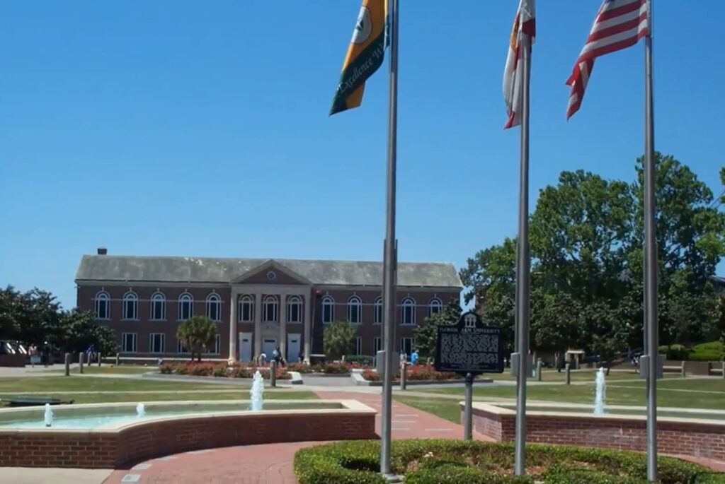 A sunny view of a historic university building with a fountain and flags
