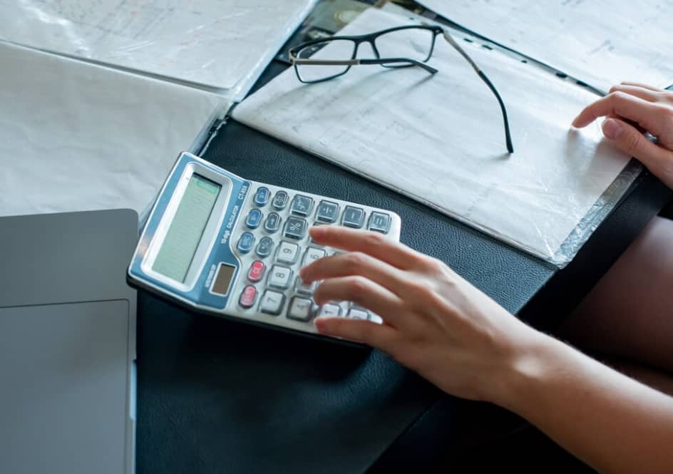 Hands using a calculator next to a laptop and documents