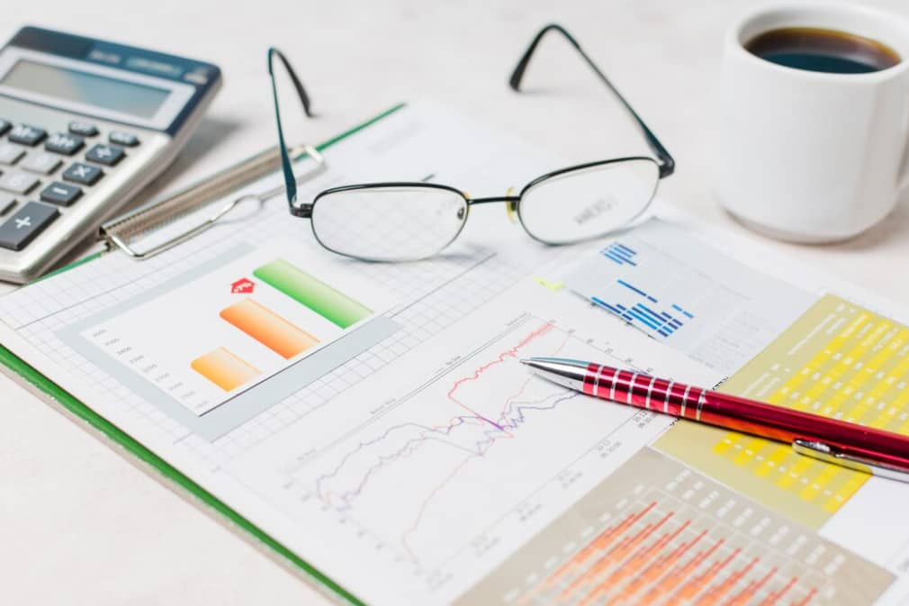 A desk with a calculator, glasses, and financial charts