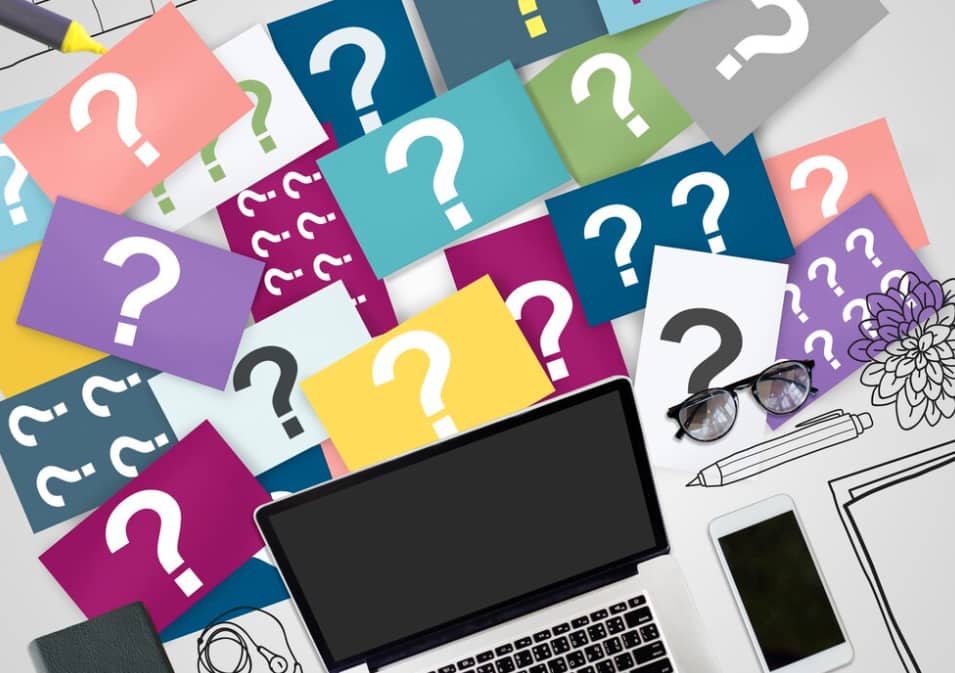 Desk with laptop surrounded by colorful question mark cards and glasses